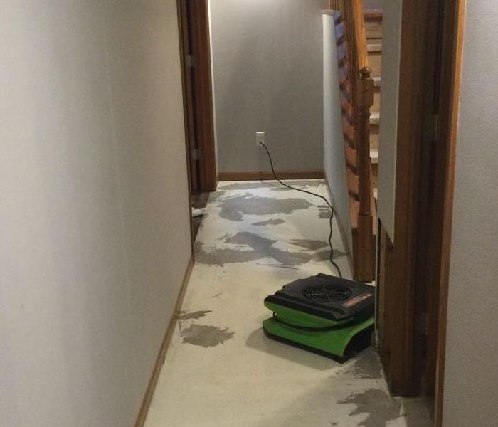 water damaged hallway with damaged floors removed and an air mover in place to dry the area