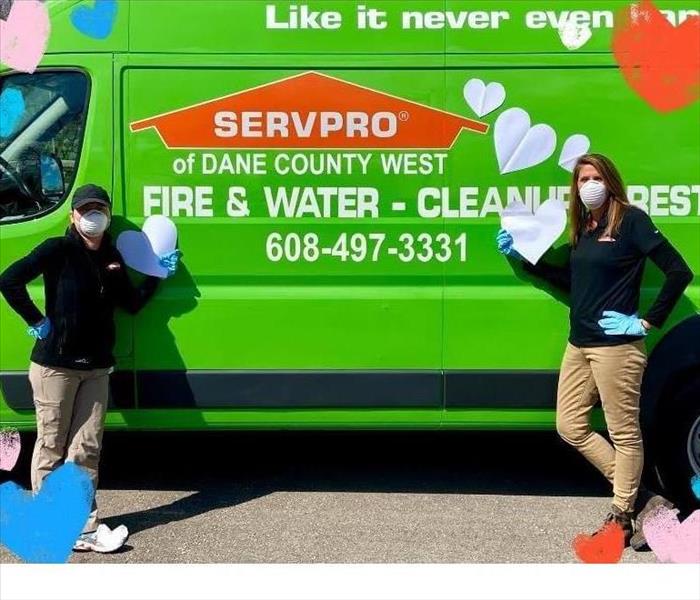 two females in SERVPRO uniforms standing in front of Green SERVPRO truck holding hearts
