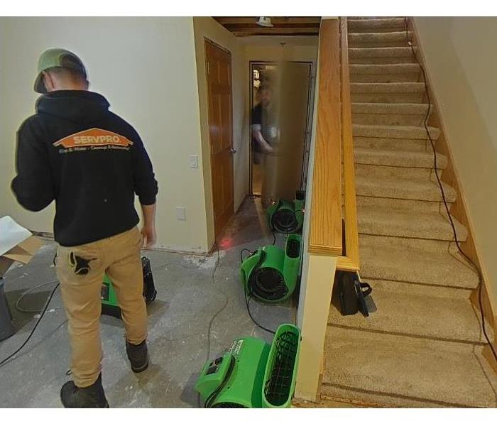 view of basement stairs leading to water damaged basement with SERVPRO professionals placing air movers to dry 