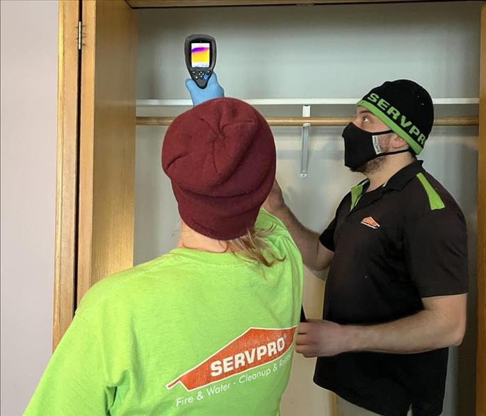 two people in servpro uniforms using an infrared camera to detect water damage in a bedroom 