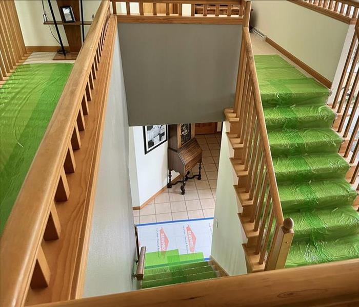 two adjoining wood stairways with carpet stairs covered in SERVPRO green plastic covering