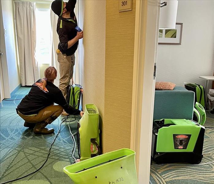 two servpro technicians using scoping tools to determine water damage of a hotel room and hallway 
