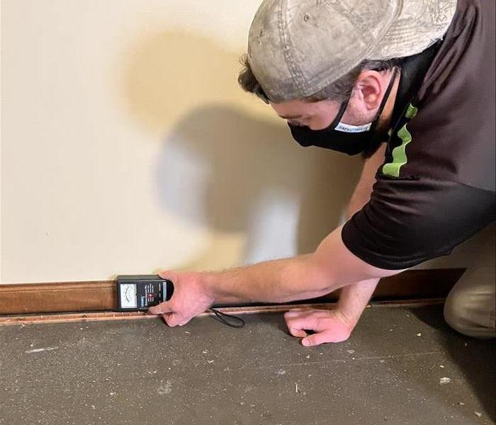 a man in a servpro uniform using a moisture meter to detect water saturation on a wall