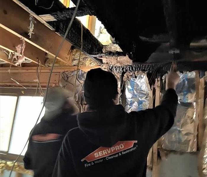 two men in SERVPRO black uniforms inspecting a fire damaged ceiling from an electrical fire