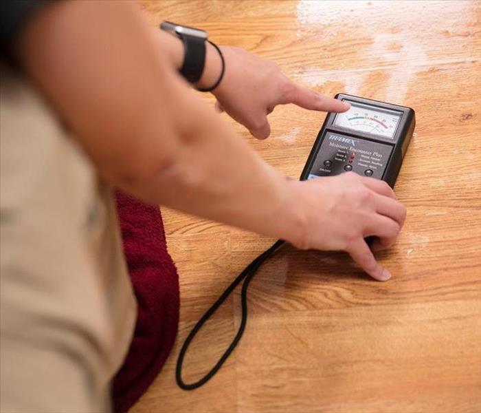 a person in a SERVPRO using a moisture meter on a water-saturated wood floor  