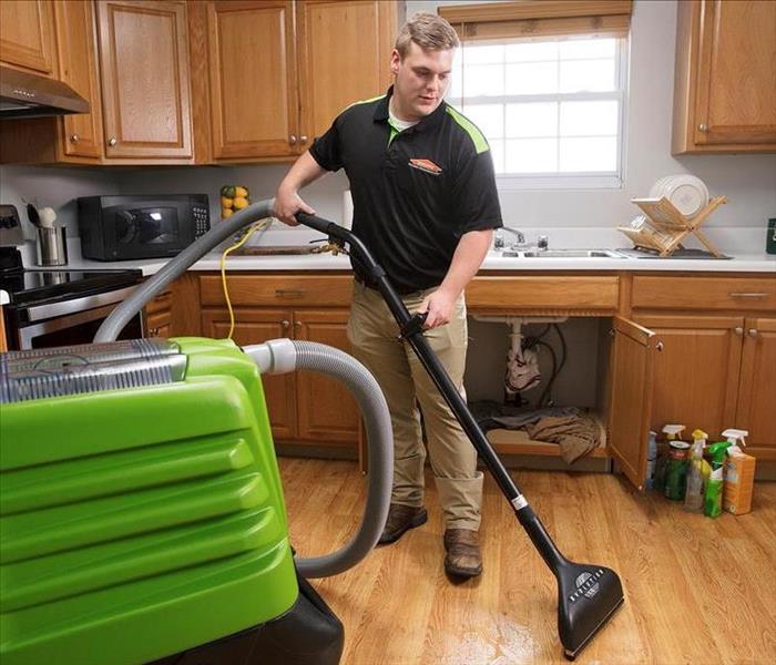 a man in a SERVPRO ready uniform using extraction equipment in a water logged kitchen to dry it