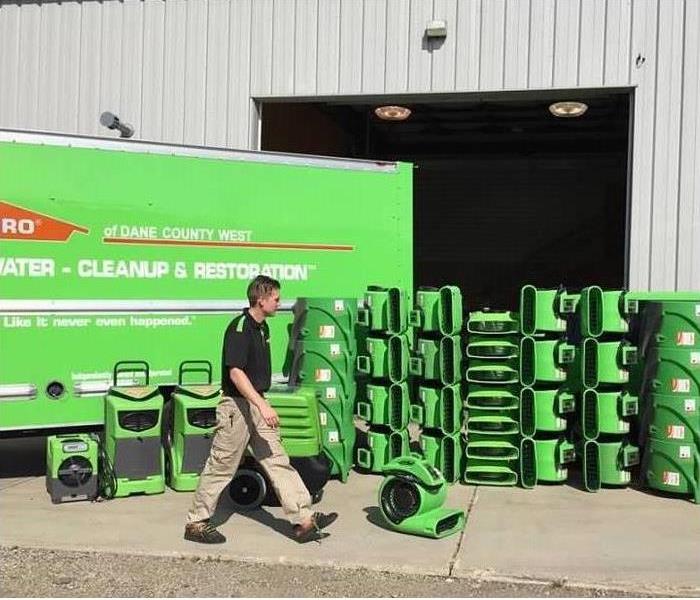 SERVPRO green truck with many stacks of green air-movers and humidifiers behind a service technician dressed in a black polo