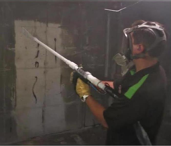 a male with brown hair in servpro ready uniform using a dry ice blasting spray machine to clean soot  from fire damage wall