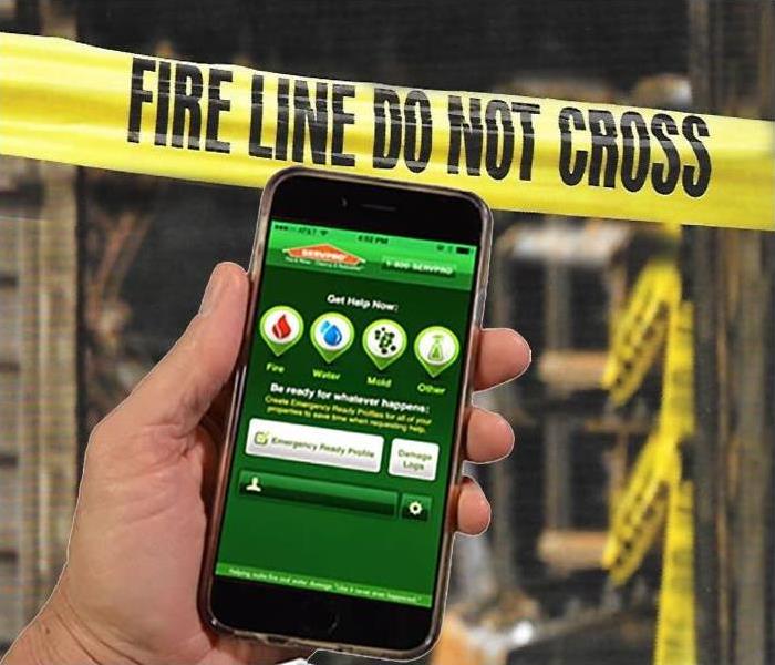 a hand holding a smart phone with SERVPRO ERP app with background of fire damage 