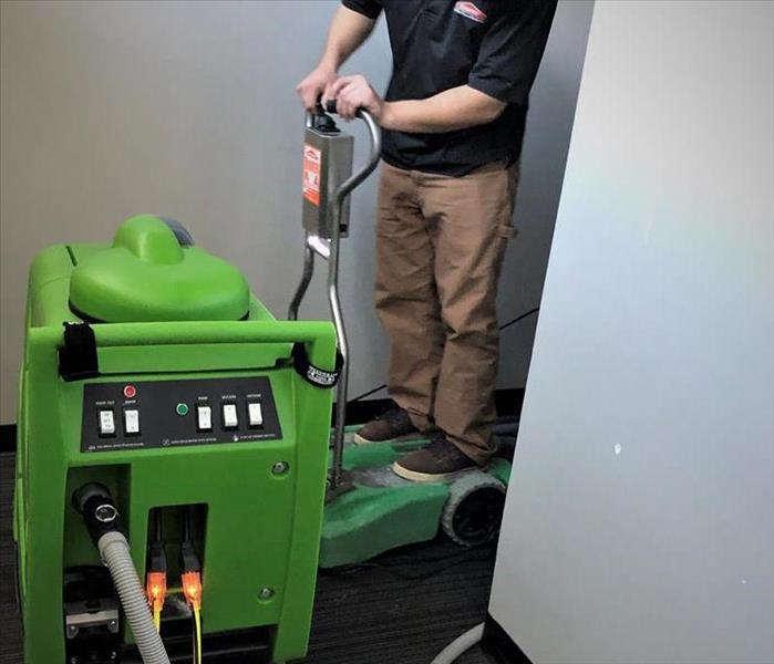 a guy in SERVPRO ready uniform on an portable extractor in an office space for a commercial water loss