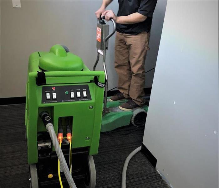 a man in a black polo and khaki pants driving a portable green water extractor hooked up to another larger water extractor